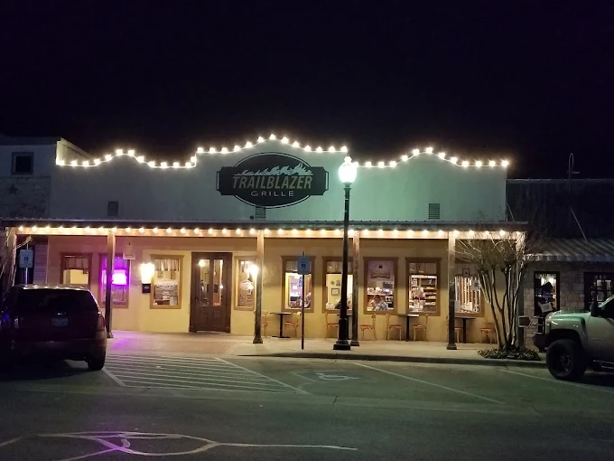 Nighttime view of Trailblazer Grille restaurant exterior, illuminated by warm lights and decorative string lights along the roofline.